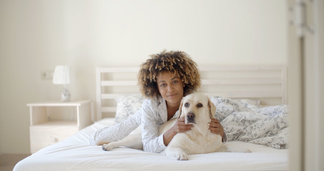 Young woman is holding a dog while laying on a bed in home