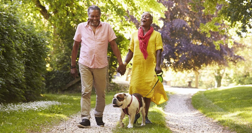 Senior Couple Walking With Pet Bulldog In Countryside