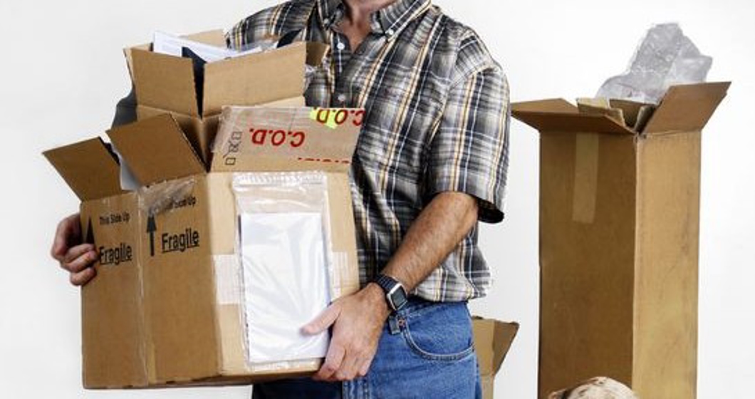 MIddle age man and dog moving out holding boxes looking sad in empty bare room.