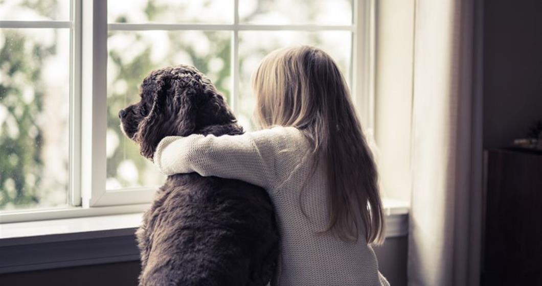 Girl watching snow out the window with her dog