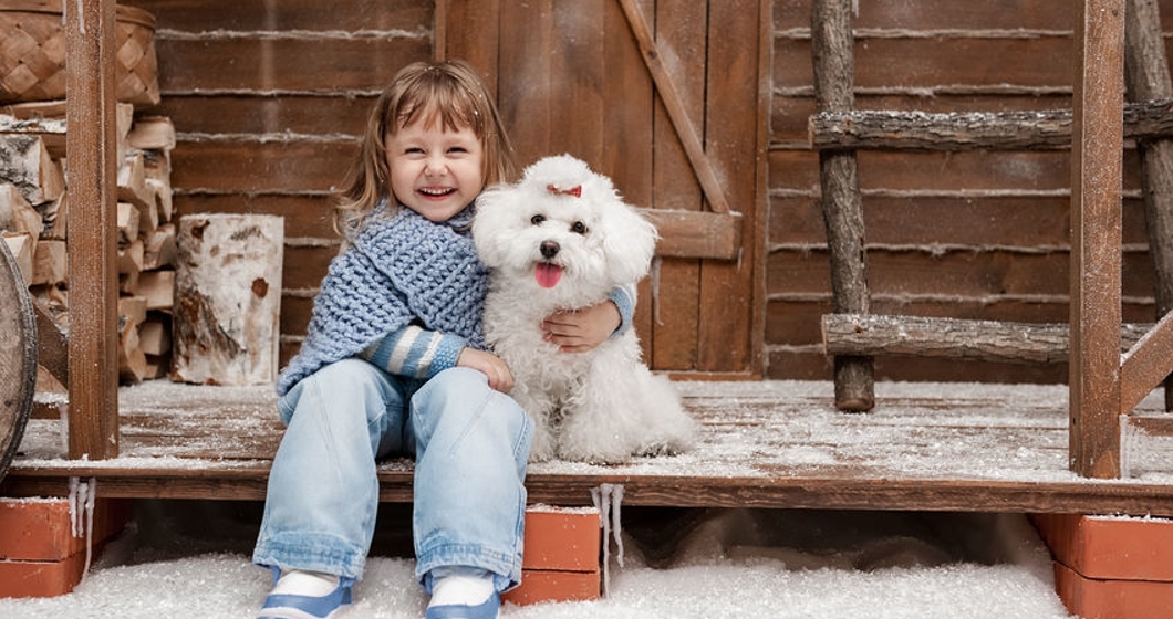 Little girl with white dog on snowy porch